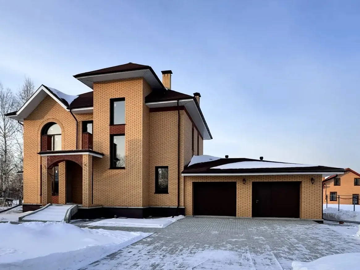 Two-story brick home with an arched entrance and garage in winter